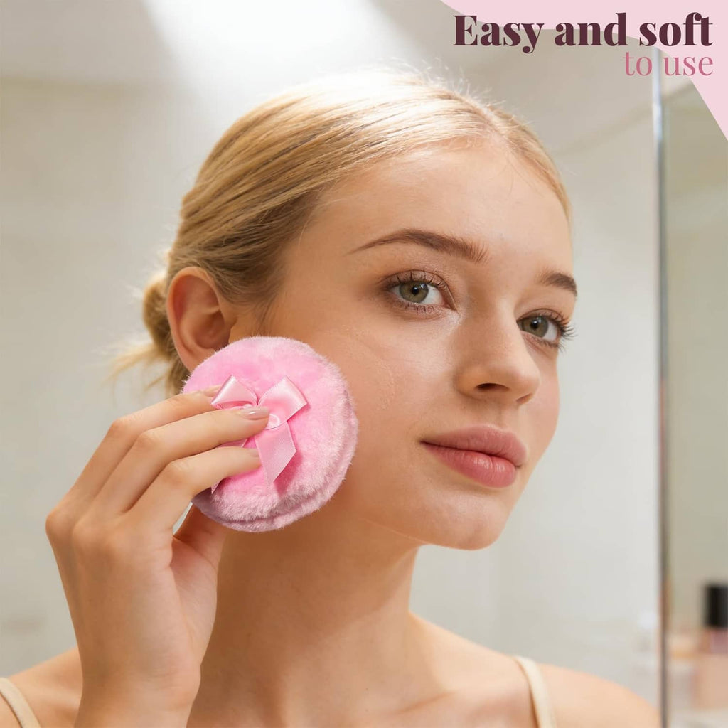 Pink round fuzzy powder puff with satin bow, held near the cheek