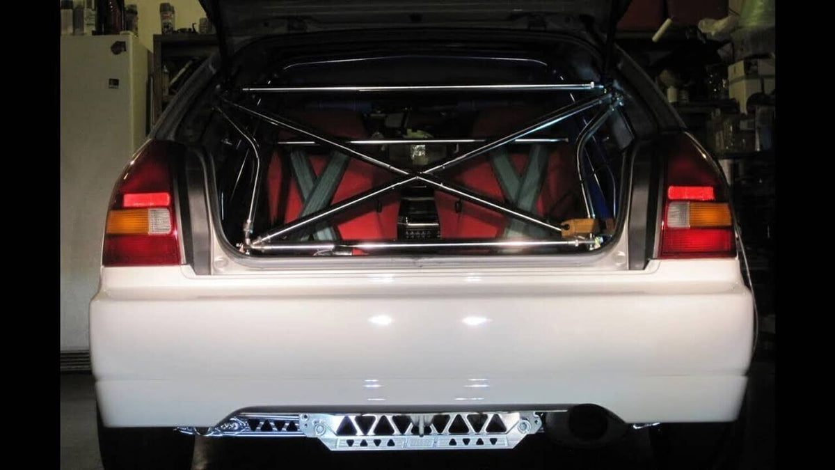 Rear subframe brace tie bar installed beneath a car, with multiple triangular cutouts