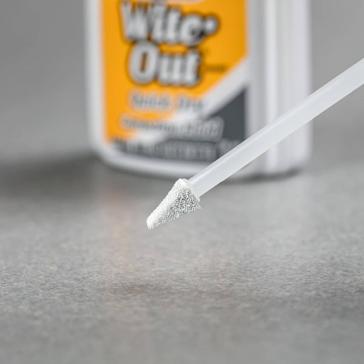 White correction fluid applicator tip dispensing a small spot on surface
