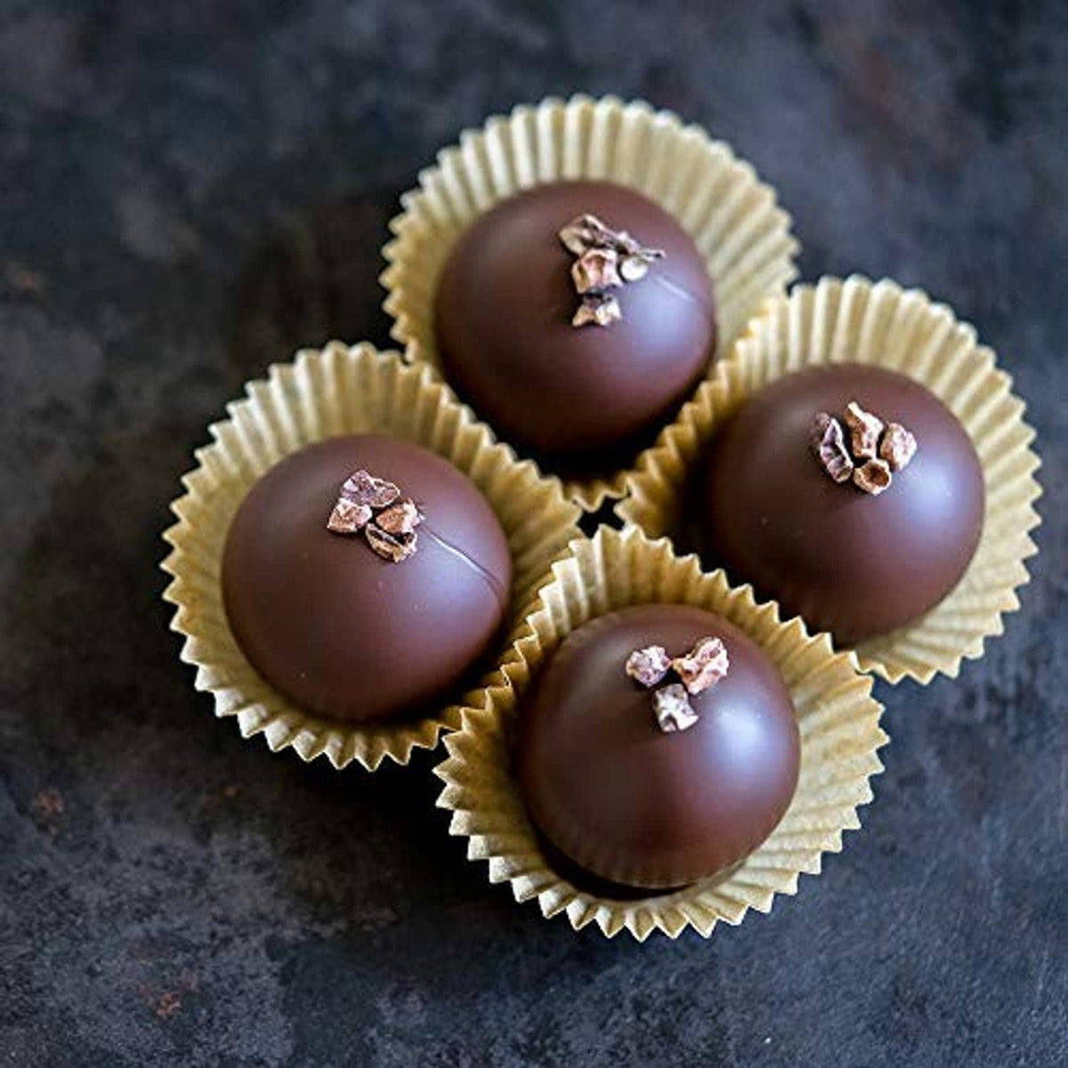 Round dark chocolate spheres in paper cups with small nut or candy topping pieces