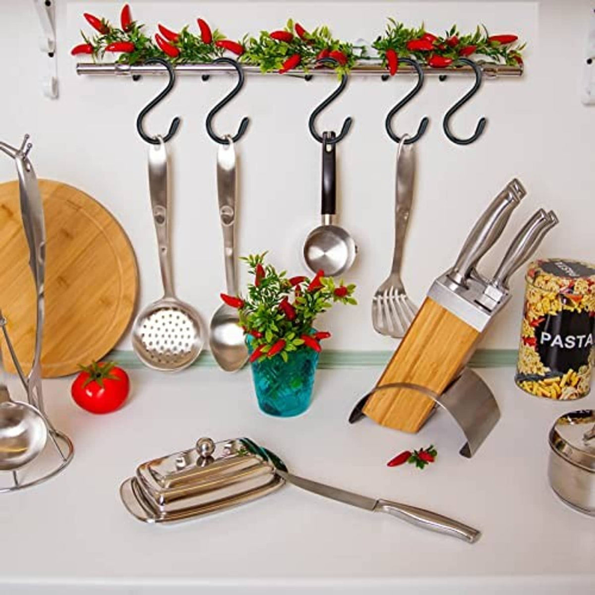 Black S hooks on wall-mounted rack, holding cooking utensils and tools by loops.