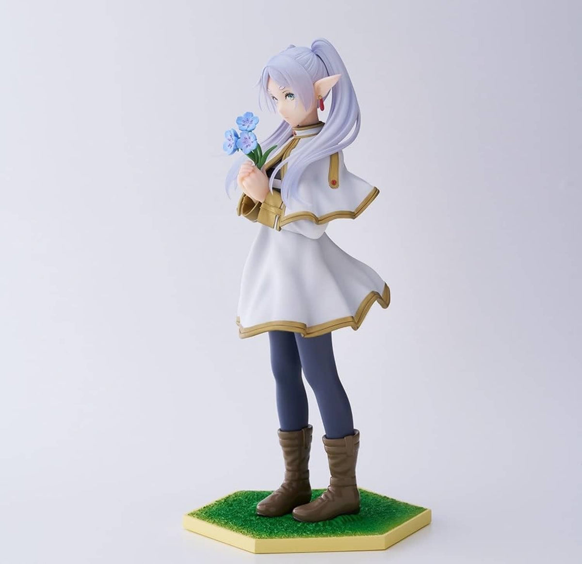 Side-view character figurine with lavender hair, white-and-gold outfit and boots, green base.