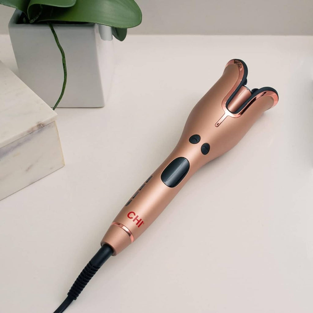 Rose gold rotating curling iron with black handle buttons and heated U-shaped barrel