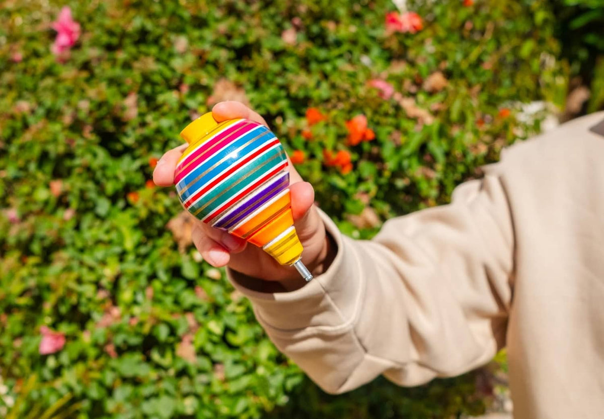 Multicolor striped wooden spinning top held in hand, yellow base and blue cap