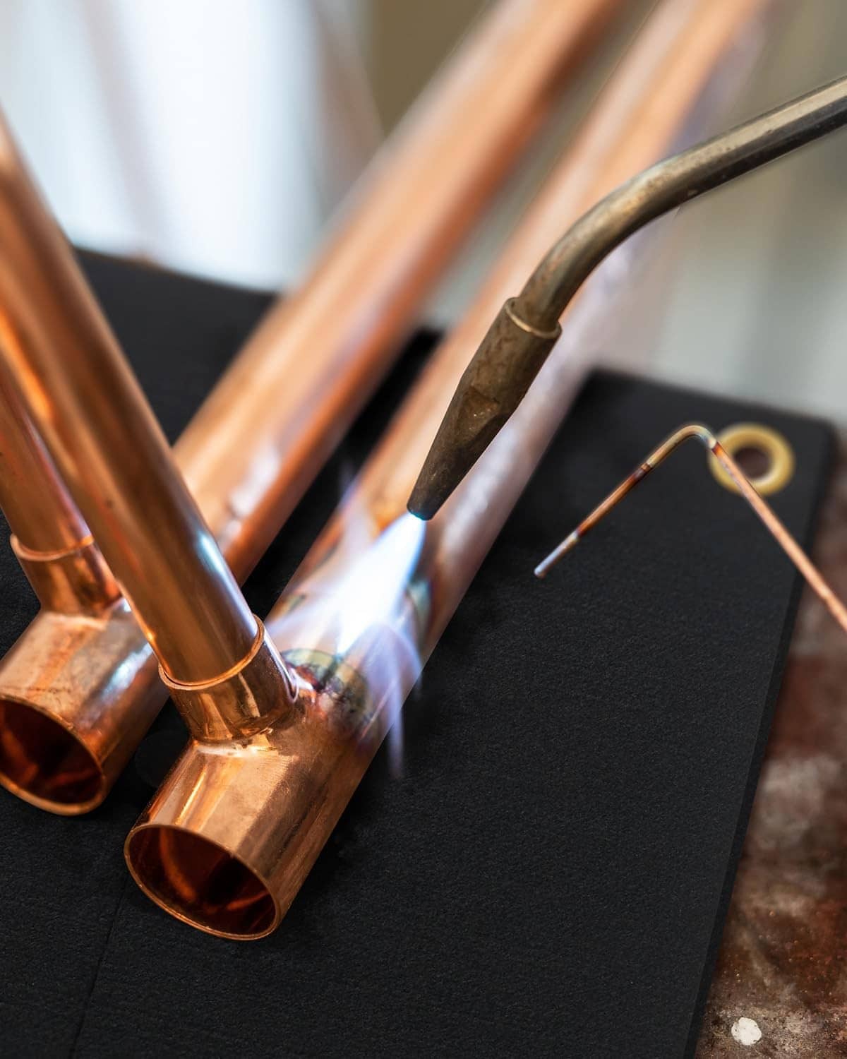 Black fireproof soldering heat shield mat beside copper pipes and torch
