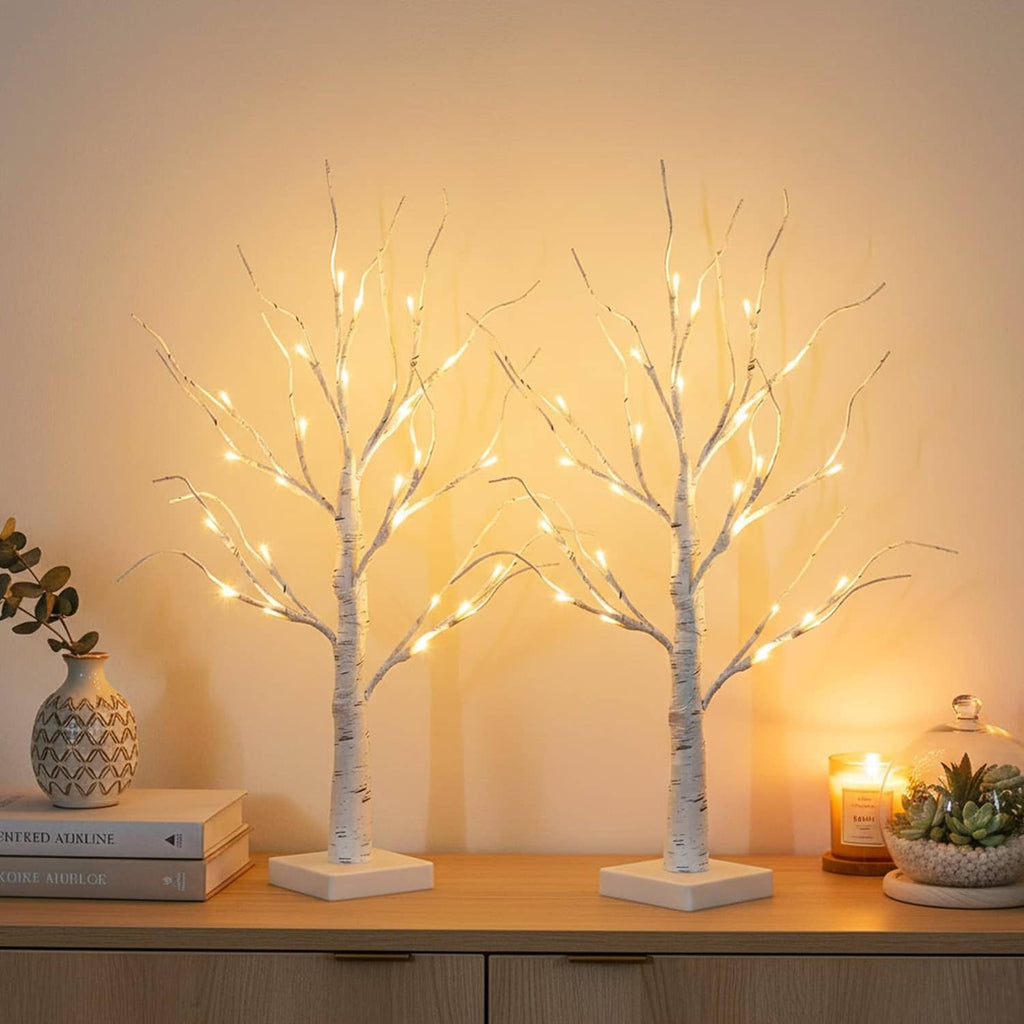Two white LED birch tree decorations with warm lights on square bases on a table