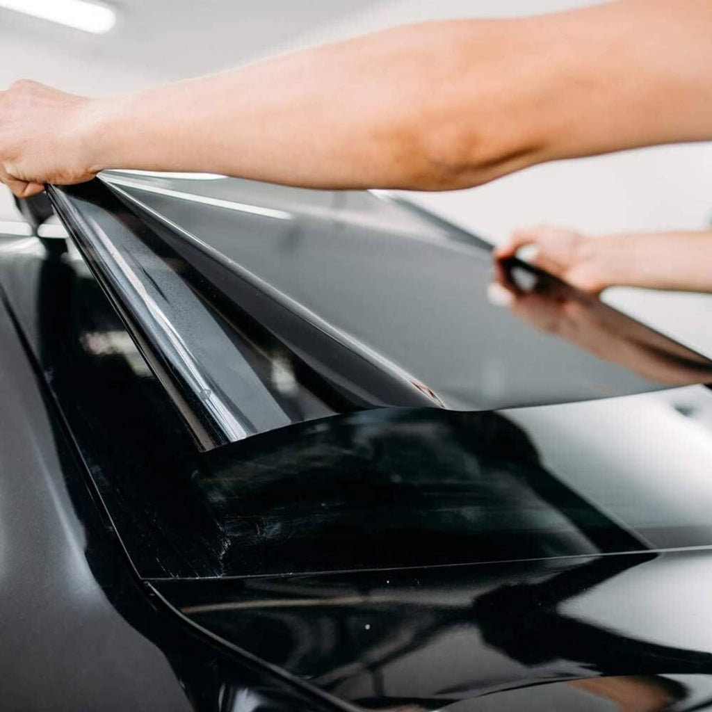 Hands smoothing a strip of dark window tint film on car glass