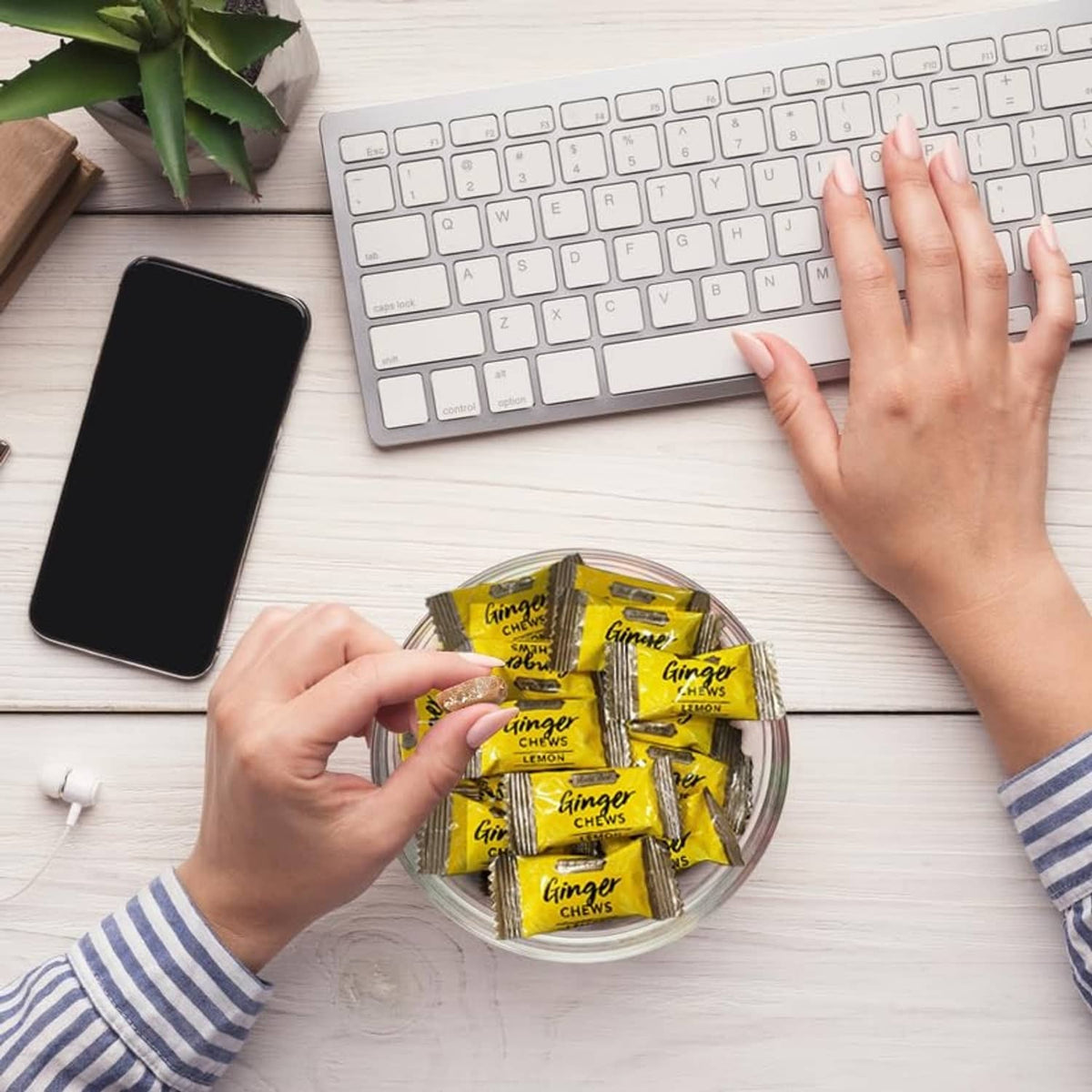Hands holding zesty lemon ginger chew packets by a keyboard on a table