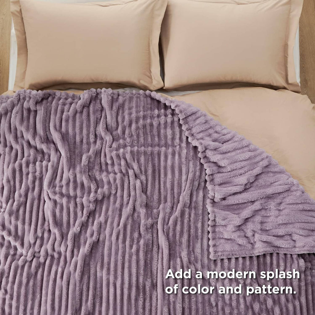 Lavender ribbed fleece blanket laid across a bed with beige pillows