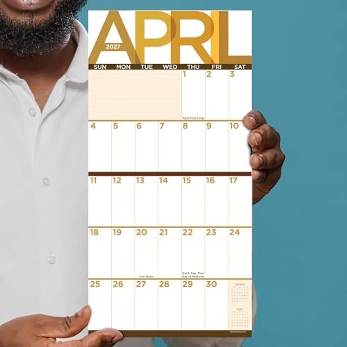 April 2027 monthly calendar sheet held in hands, showing Sunday to Saturday grid