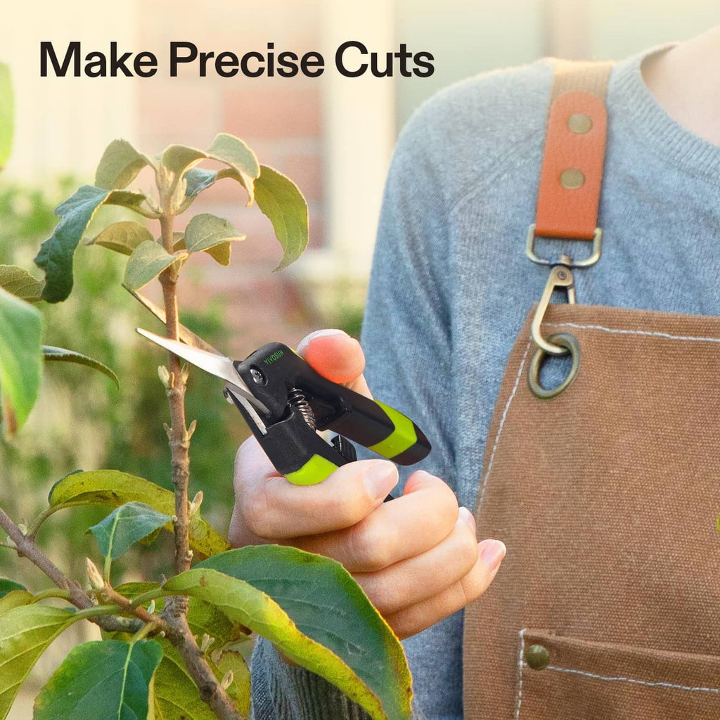 Garden scissors in hand with black body and green handles, cutting near leaves