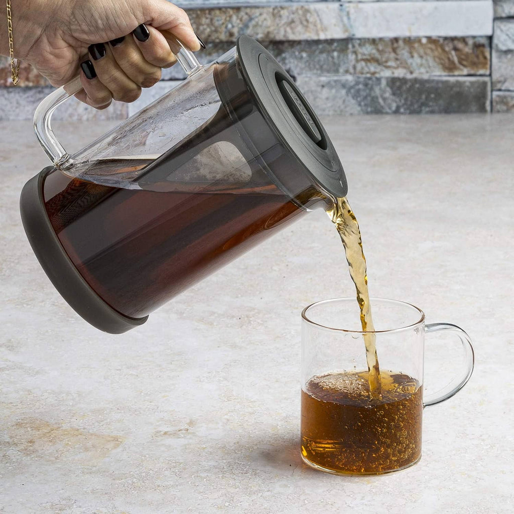 Pouring coffee into clear glass pitcher of cold brew coffee maker with black lid