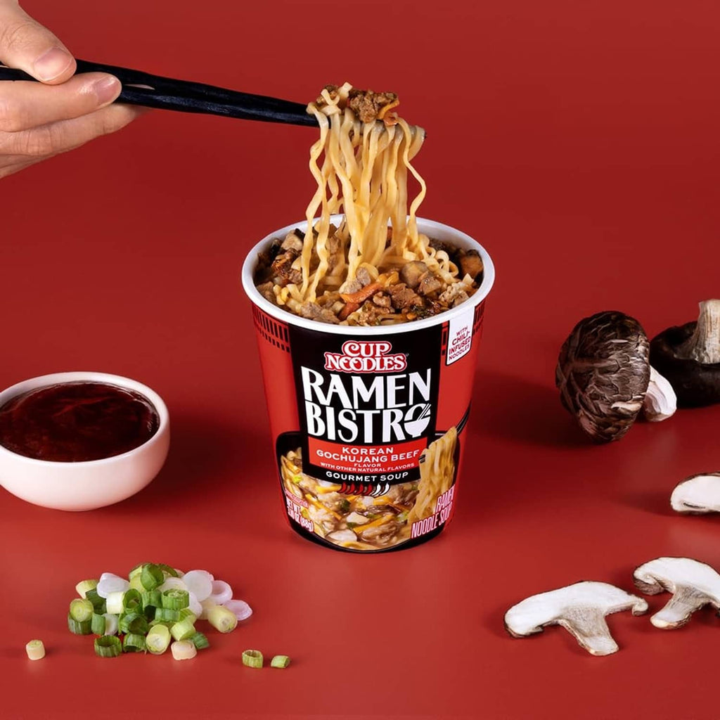 Hand lifting noodles with chopsticks above Ramen Bistro gochujang beef cup