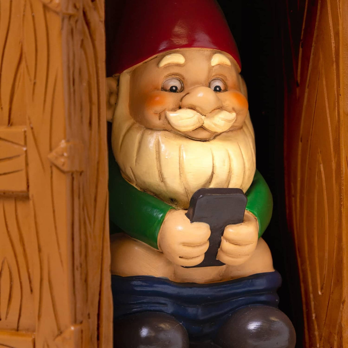 Close-up of toilet garden gnome statue face and hands, red hat, holding a dark tool