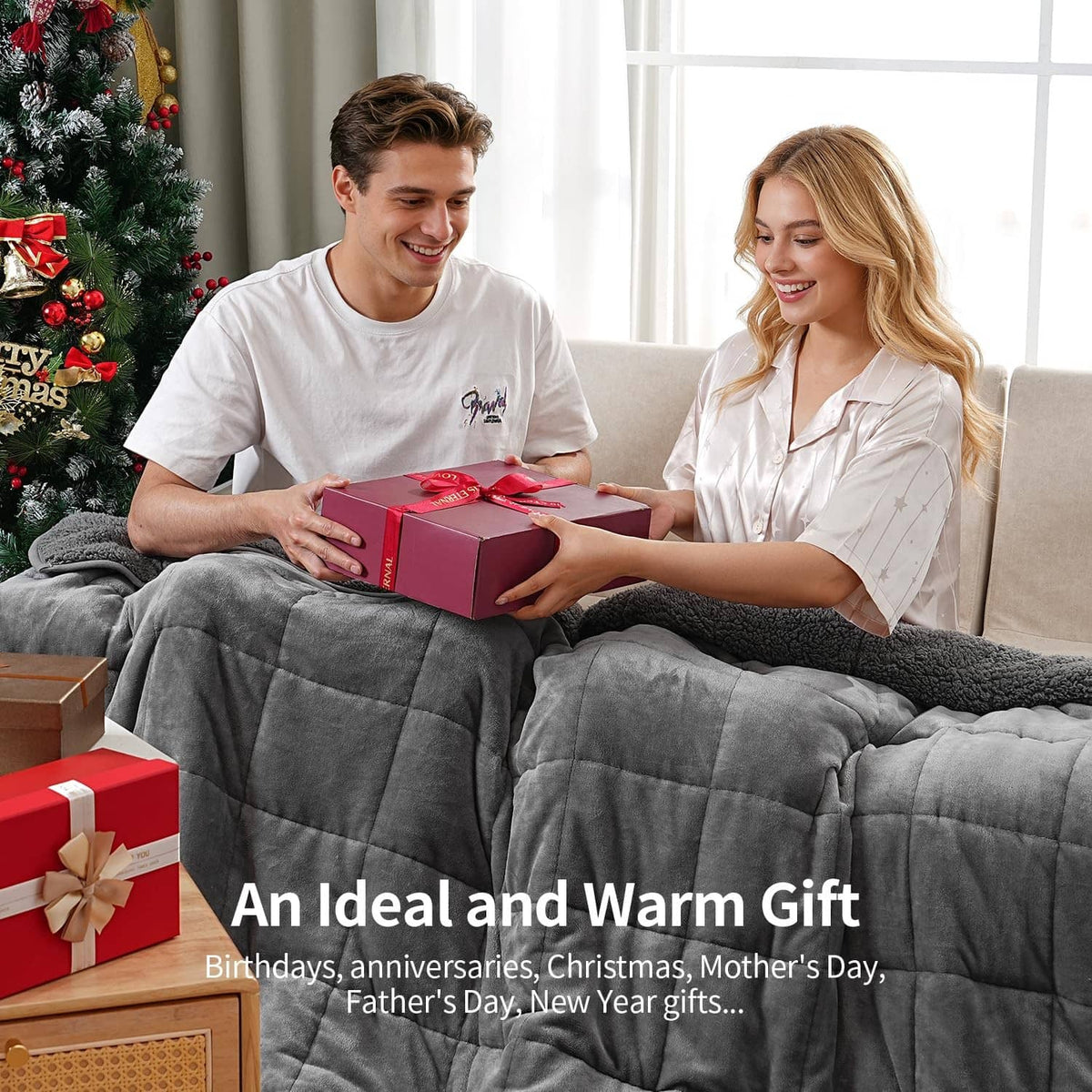Grey weighted blanket on a bed with two people holding a gift box