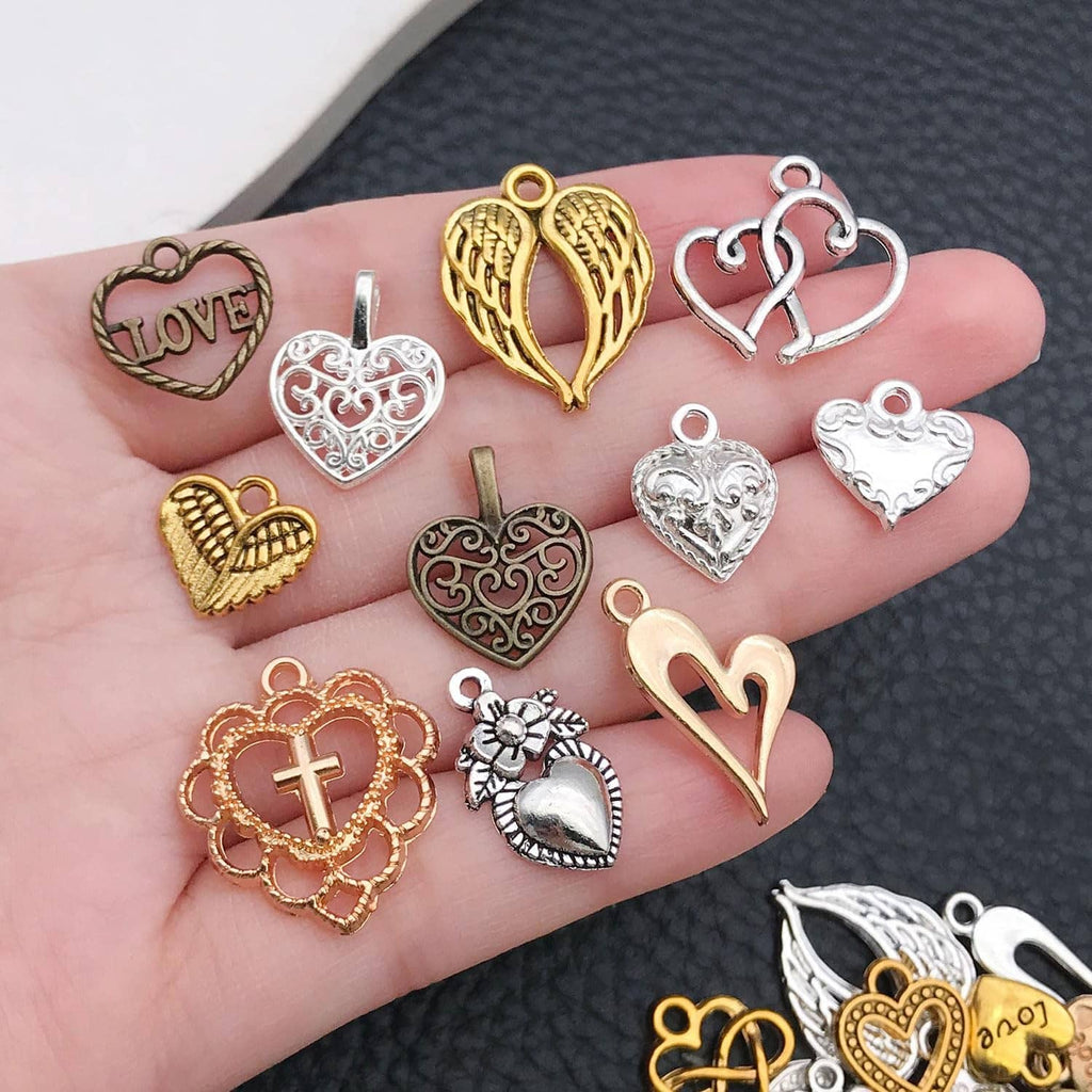 Small mixed heart charms with cross and filigree details; shown on an open palm