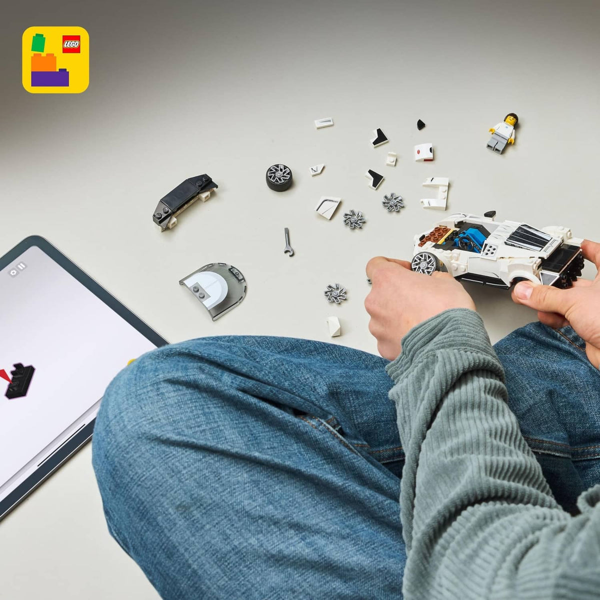 Scattered LEGO car building parts with hands assembling a white chassis