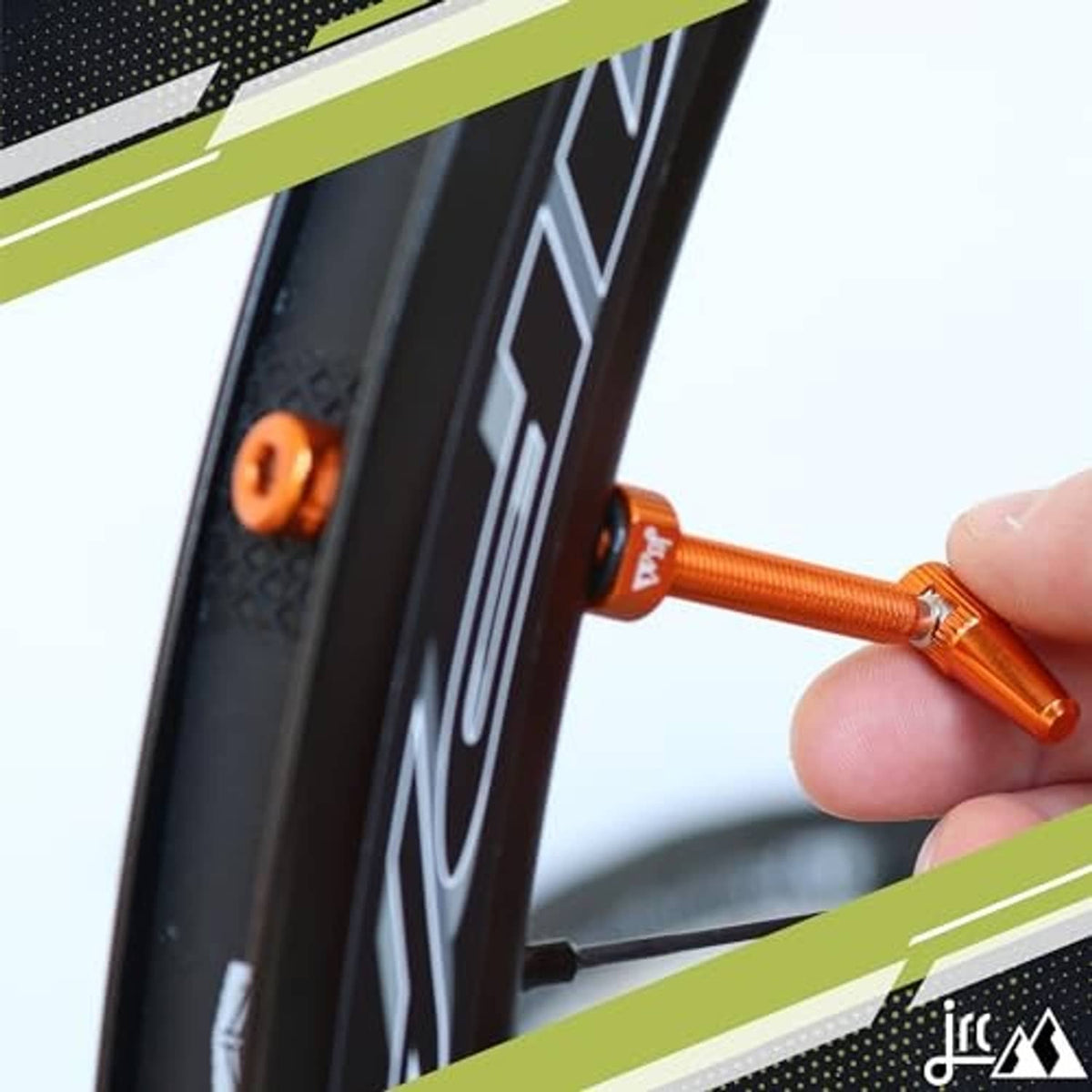 Orange anodized Presta tubeless valve stem inserted on a bicycle wheel by hand.