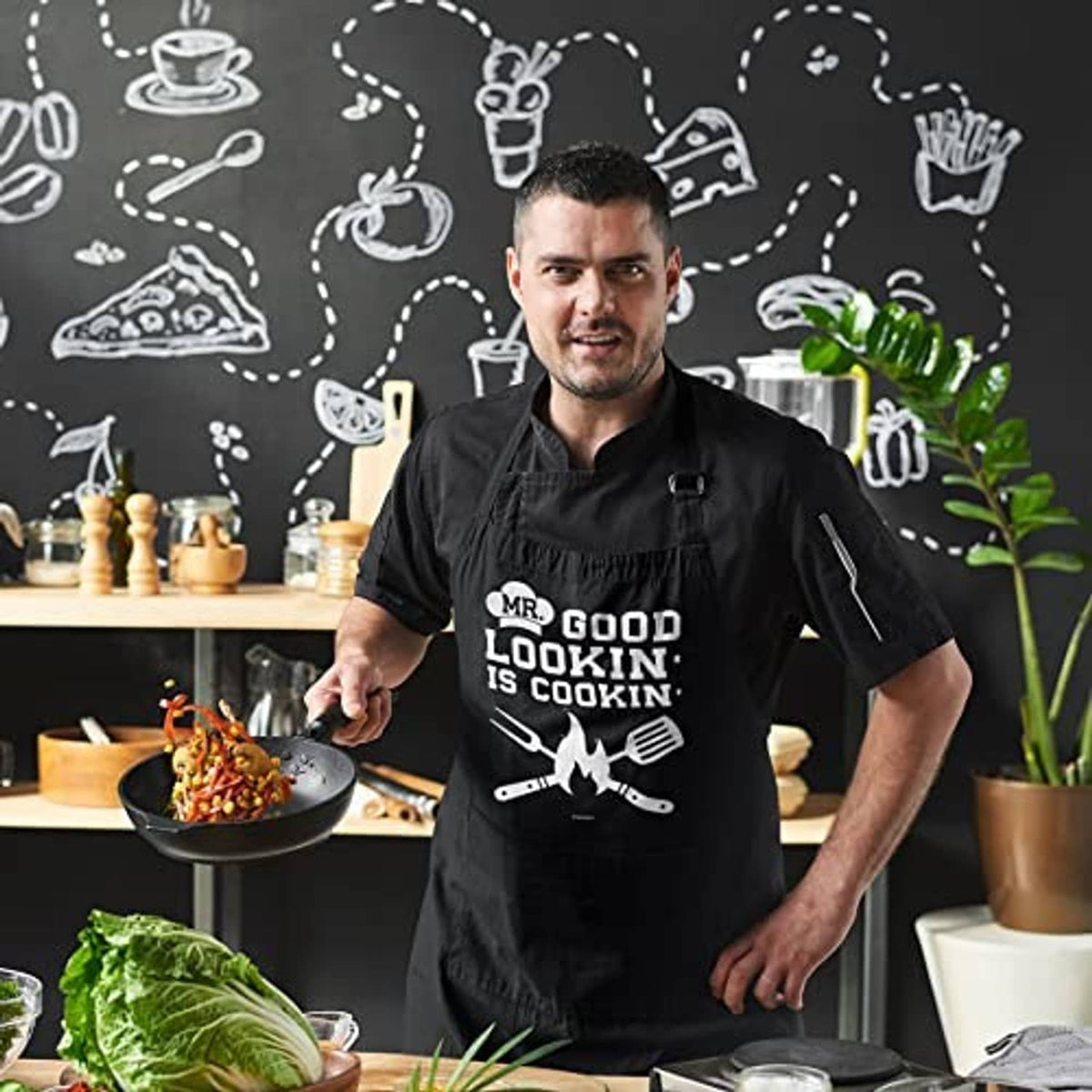 Black cotton apron with 'MR. GOOD LOOKIN' IS COOKIN' graphic, worn by cook
