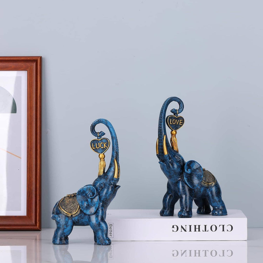 Blue elephant statue pair on white pedestal bases, with gold “LUCK” and “LOVE” emblems