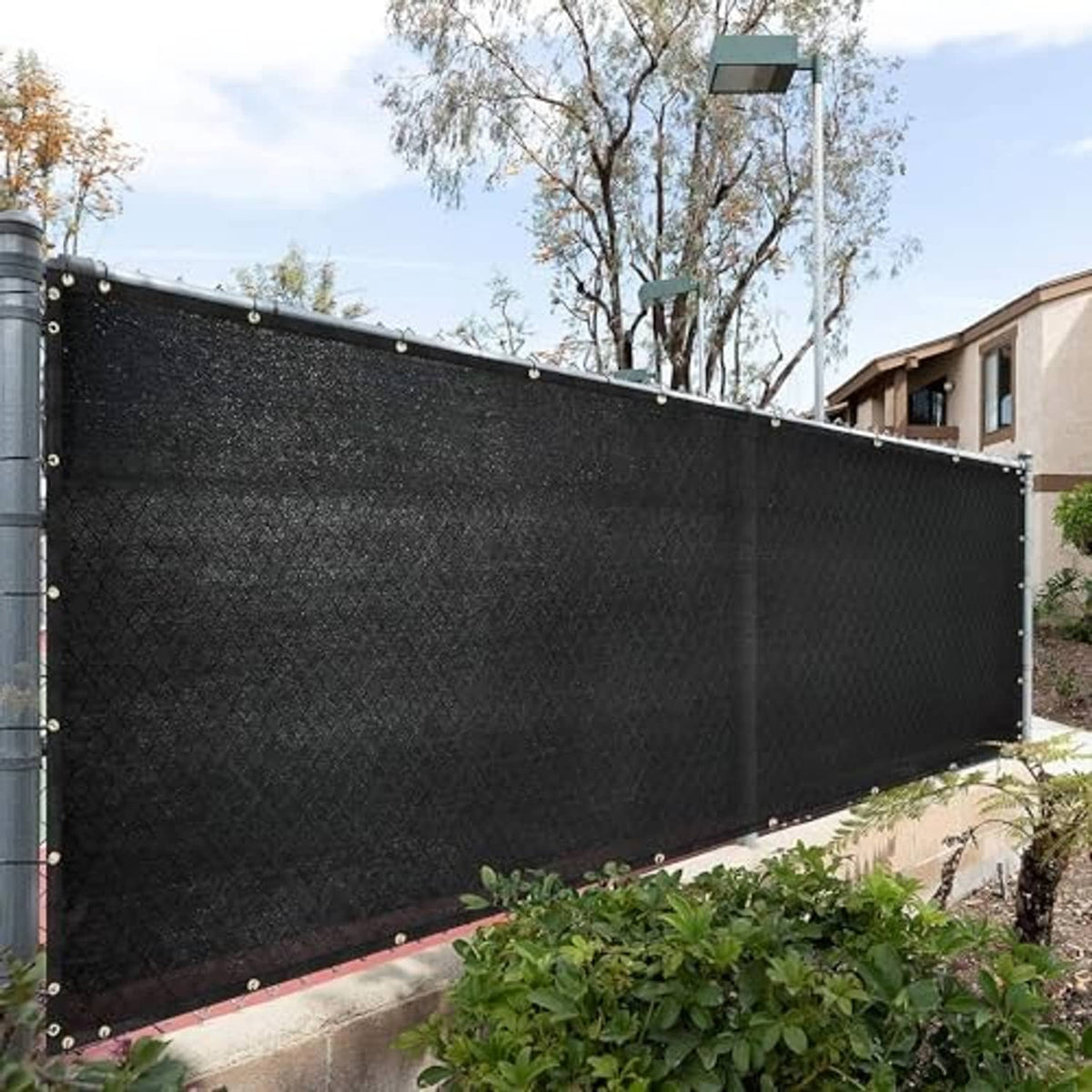 Dark mesh shade cloth panel attached along a fence line with metal grommets