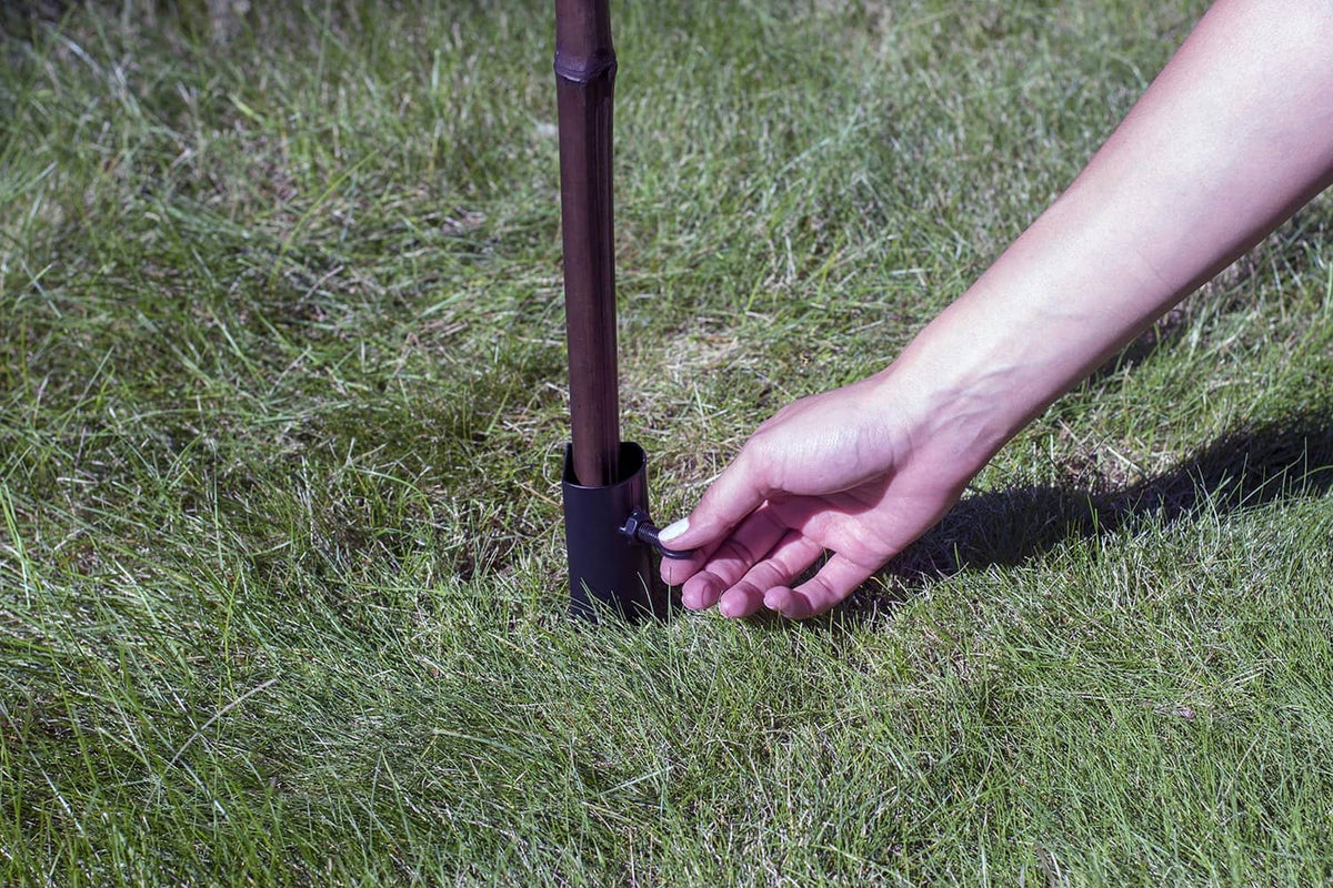 Hand pressing a black metal torch stake into the lawn