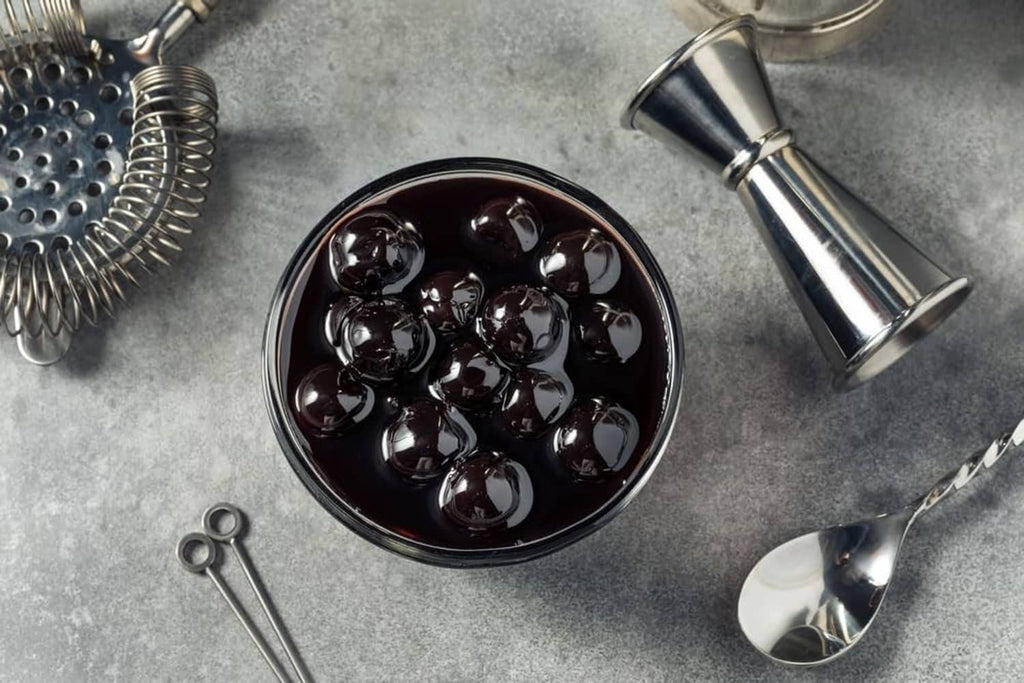 Overhead view of dark maraschino cherries in a bowl with bar tools nearby