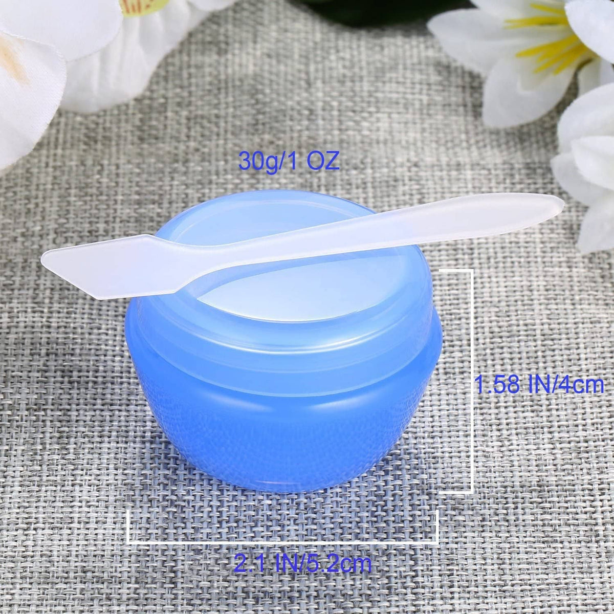 Blue 1 oz plastic toiletry jar with open lid and white scoop on fabric