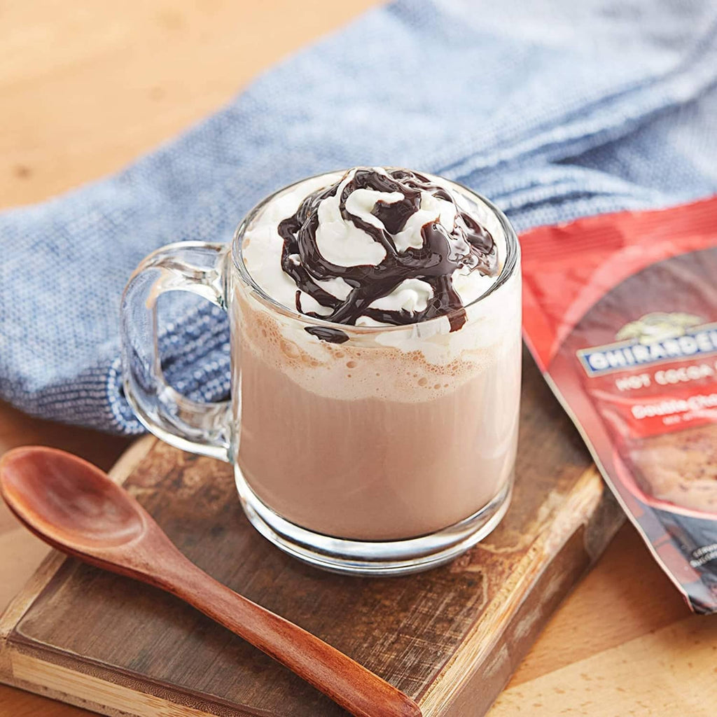 Glass mug of creamy hot cocoa with whipped topping and a mix pouch