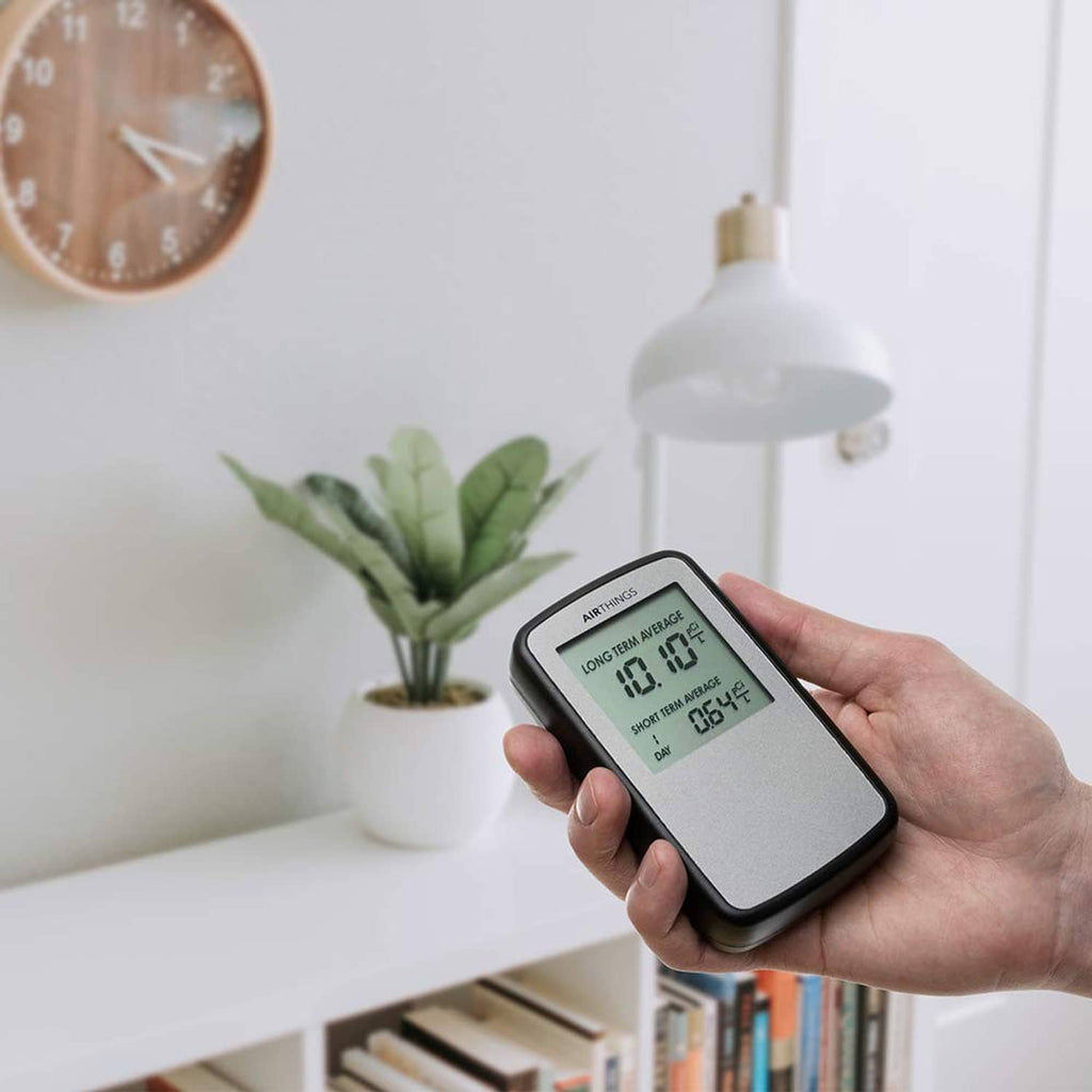 Hand holding black portable radon detector with LCD showing radon averages
