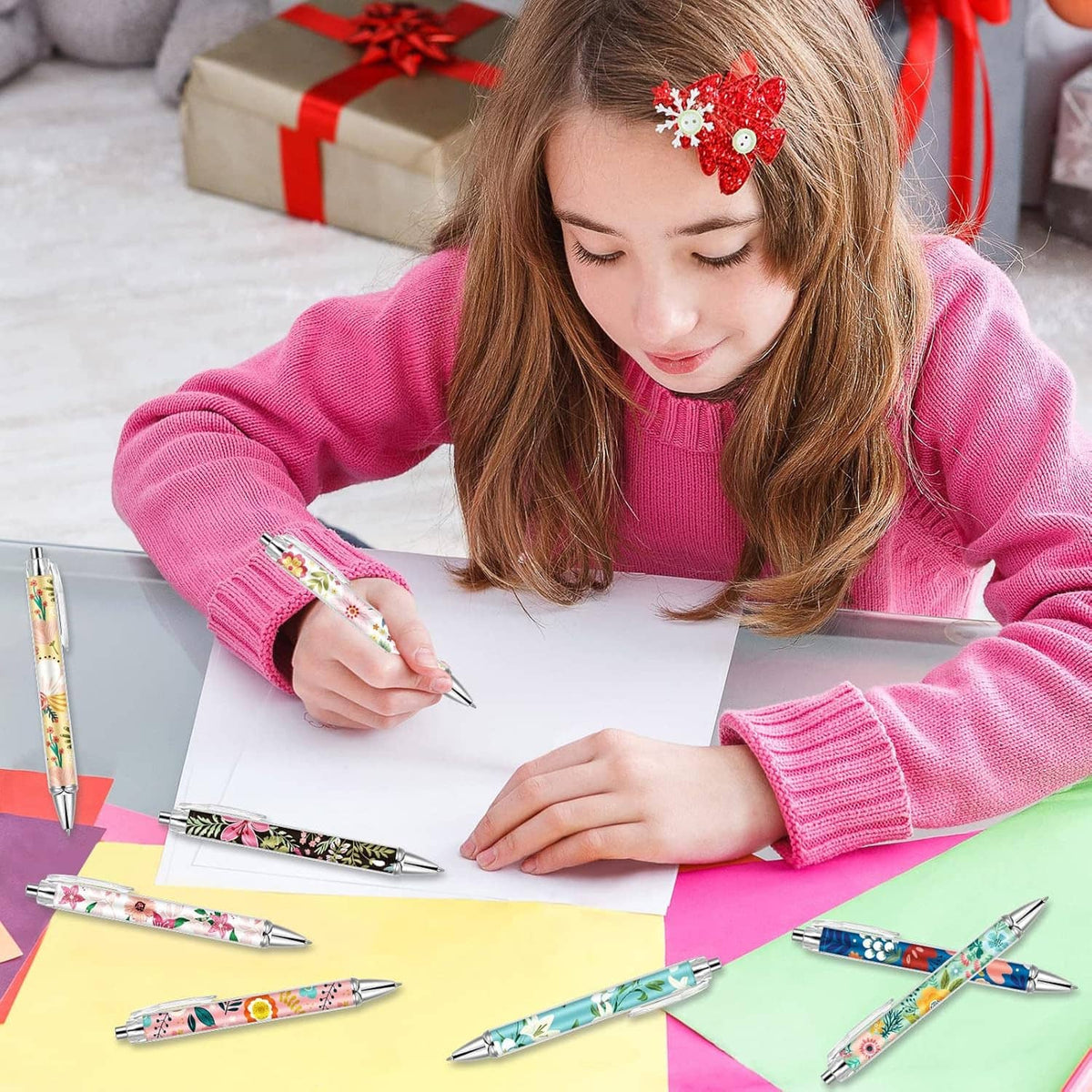 Child drawing with a floral ballpoint pen on paper, several pens nearby