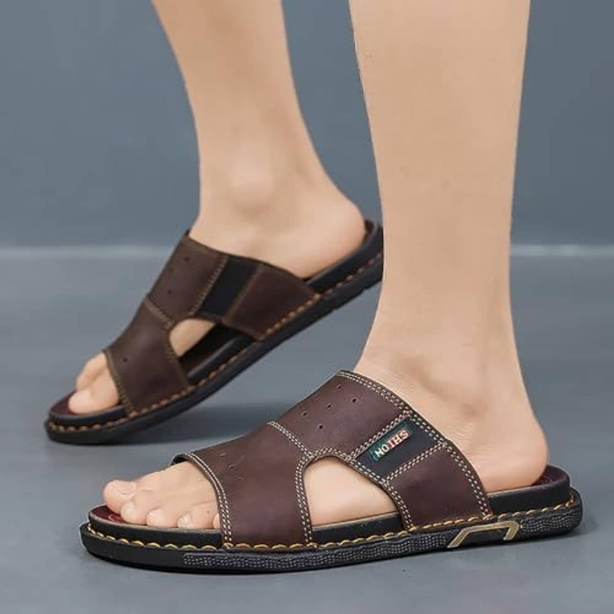 Pair of men's brown leather open-toe slip-on sandals on feet with dark cushioned sole