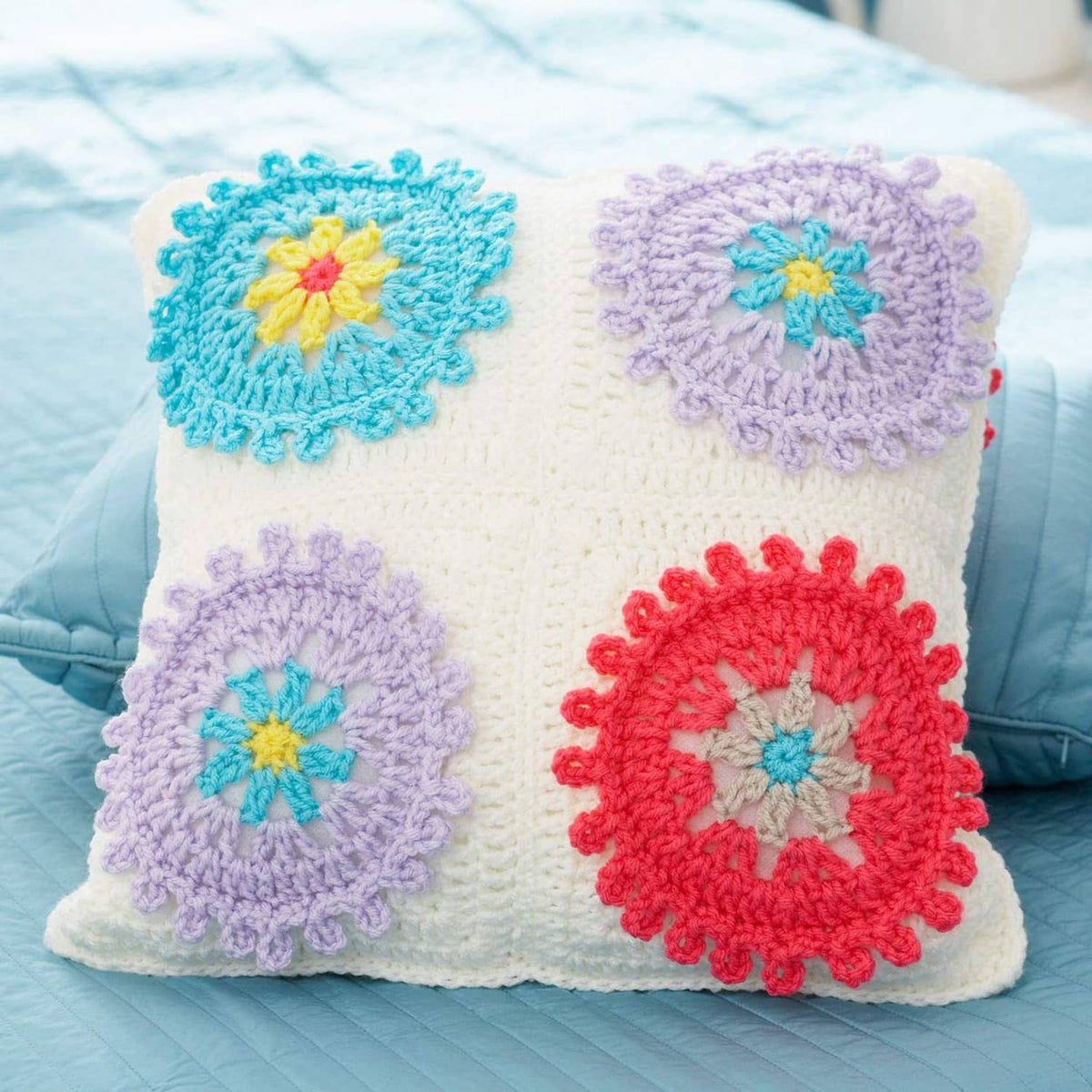 Crocheted square pillow cover with colorful flower appliques and scalloped trim