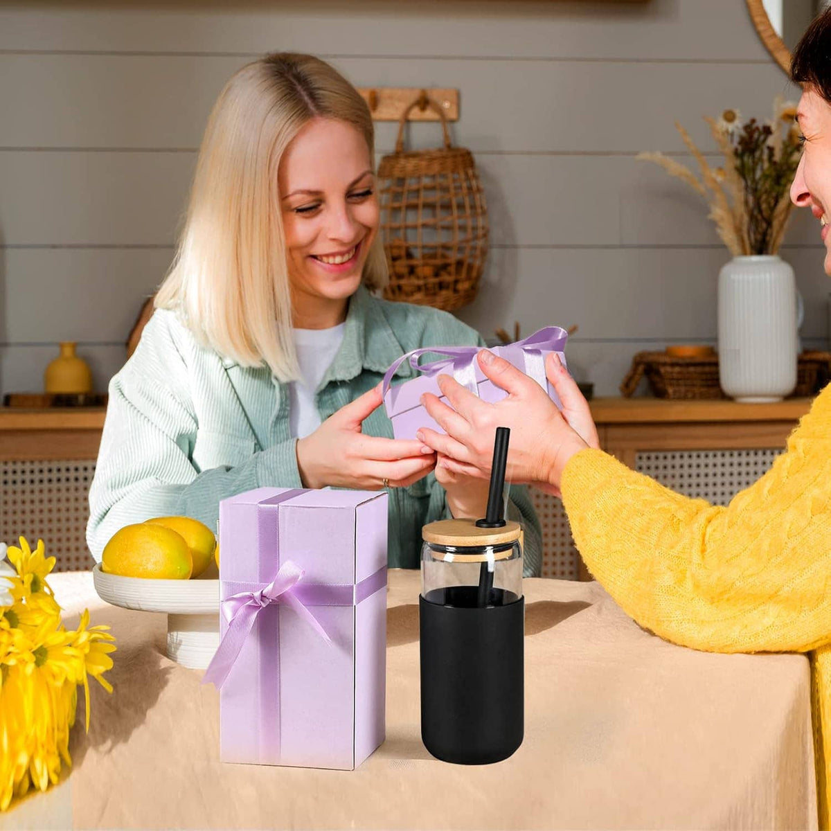 Black silicone-sleeved glass tumbler with straw beside a wrapped gift