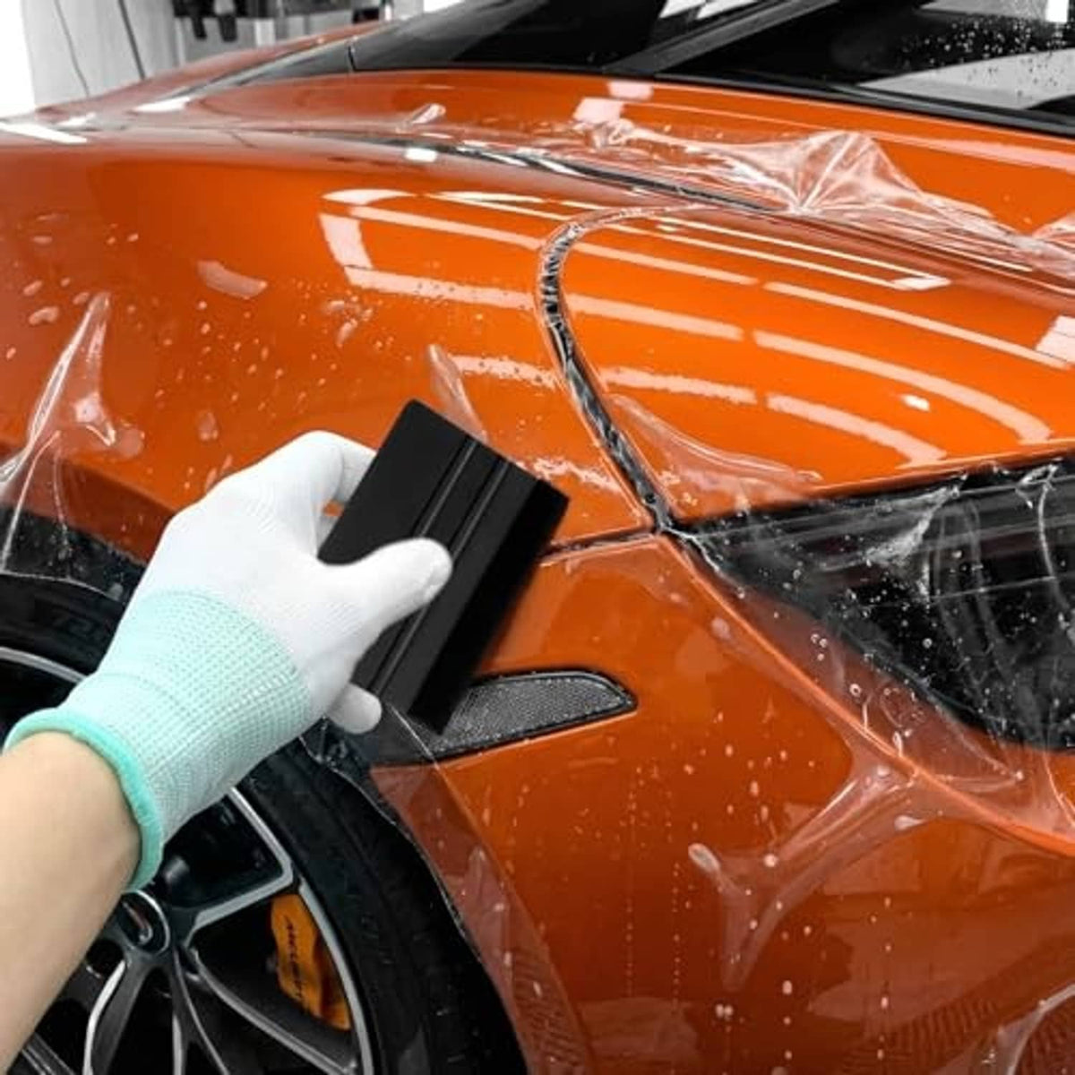 Black felt-edge squeegee pressed onto car film, with gloved hand