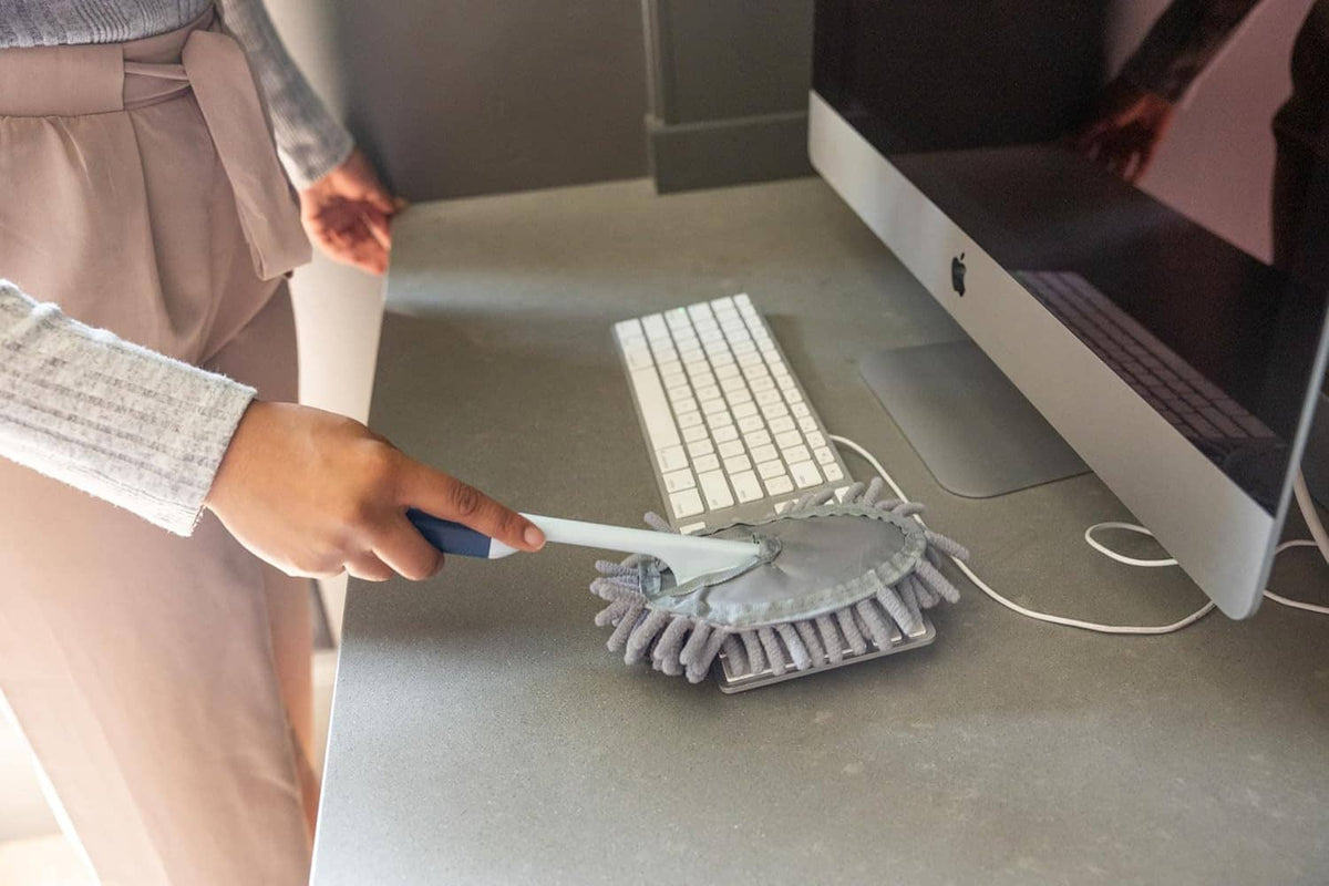 Gray handheld microfiber duster cleaning a laptop workspace