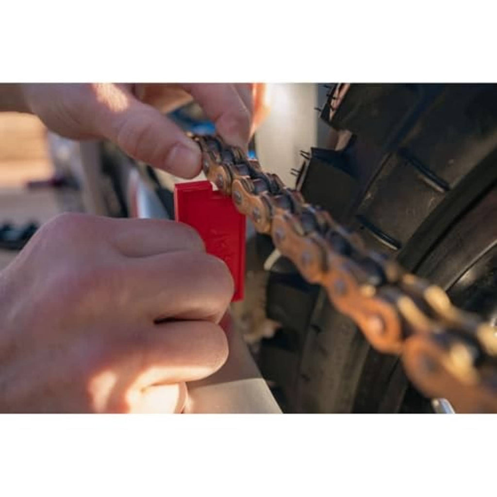 Red chain slack measuring tool applied to motorcycle chain, held by a mechanic