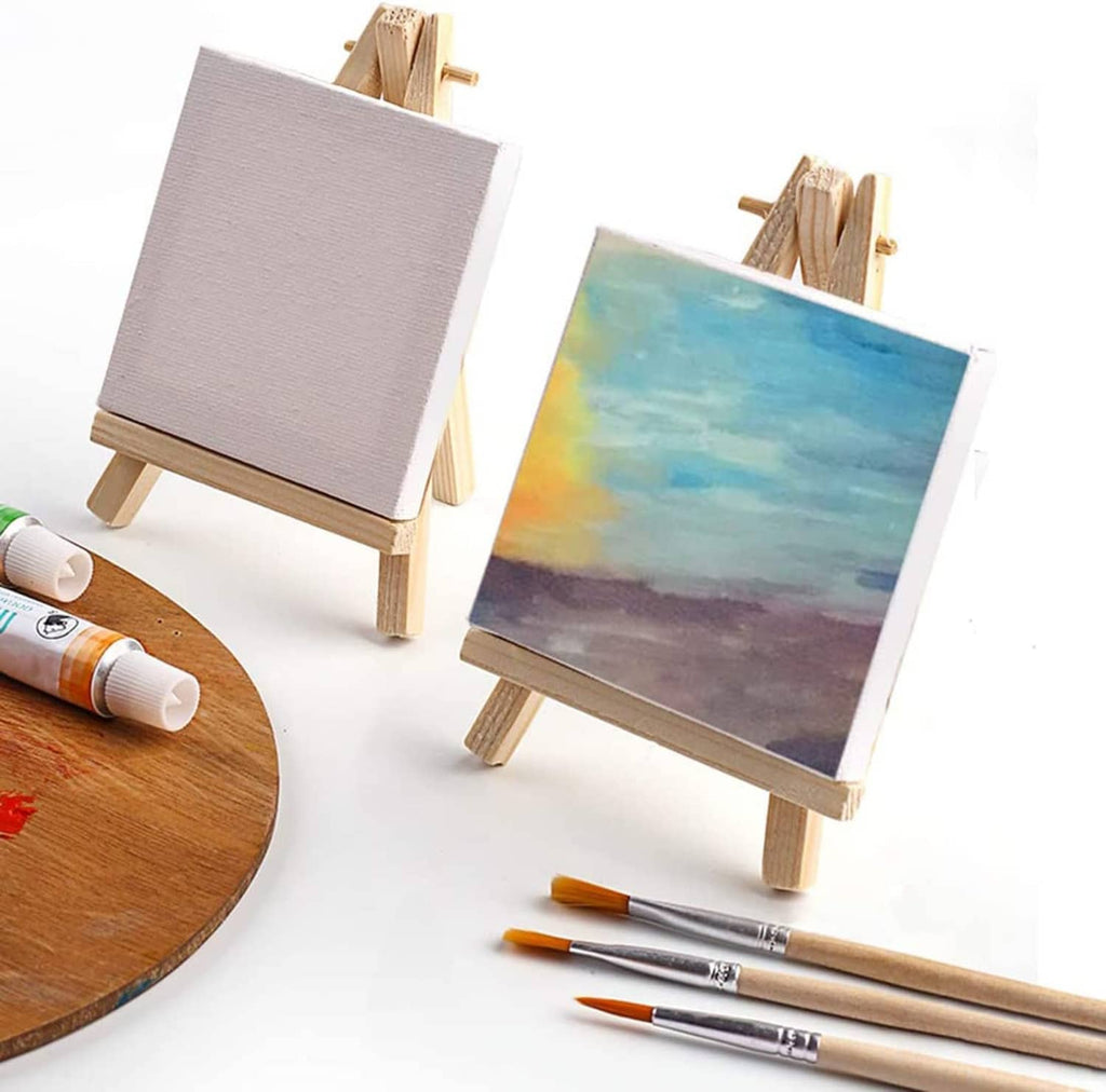 Blank mini canvas on a wooden easel with paint supplies and a painted canvas