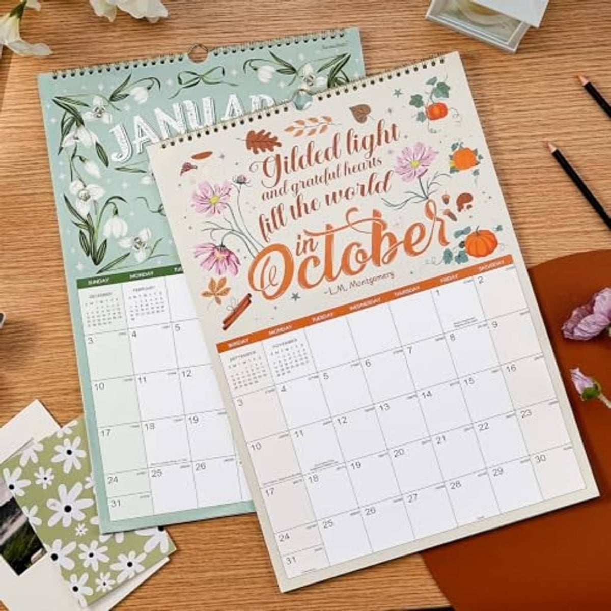 January and October 2027 wall calendars laid on desk, showing colorful month cover artwork