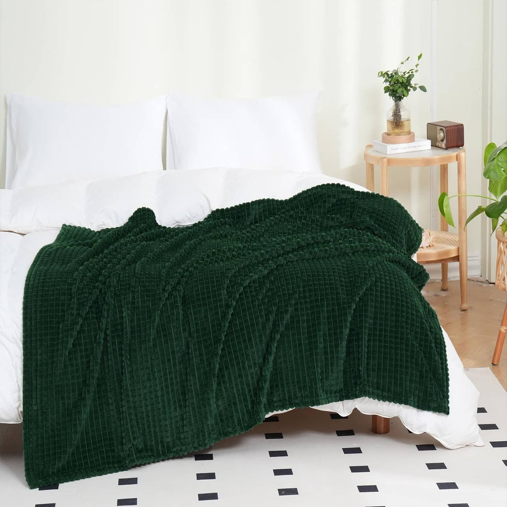 Dark green flannel fleece throw blanket, folded over white couch with textured surface