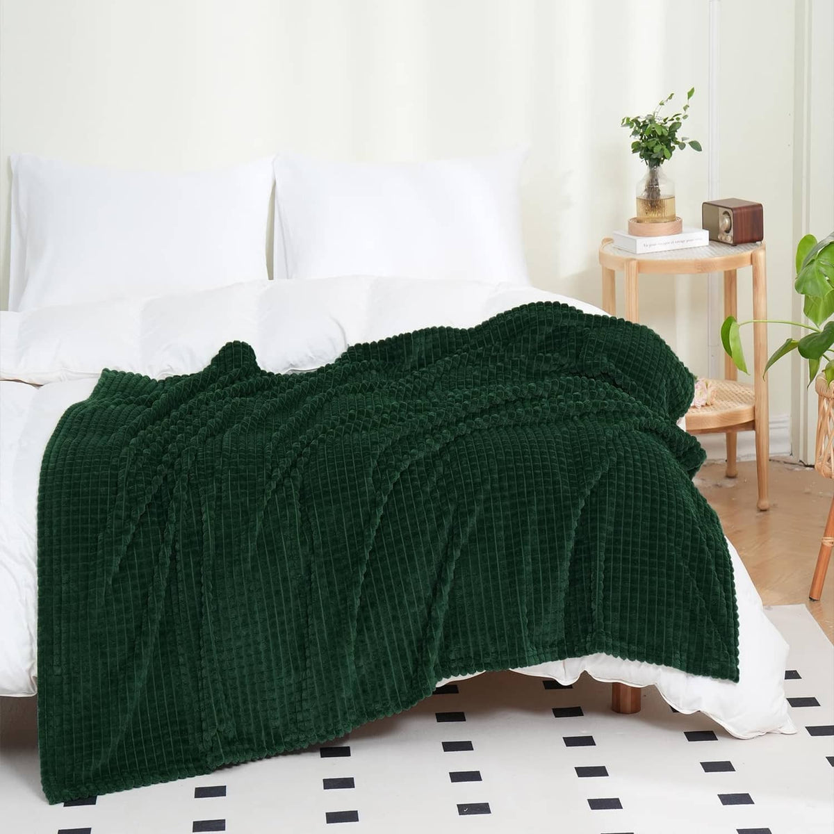 Dark green flannel fleece throw blanket, folded over white couch with textured surface