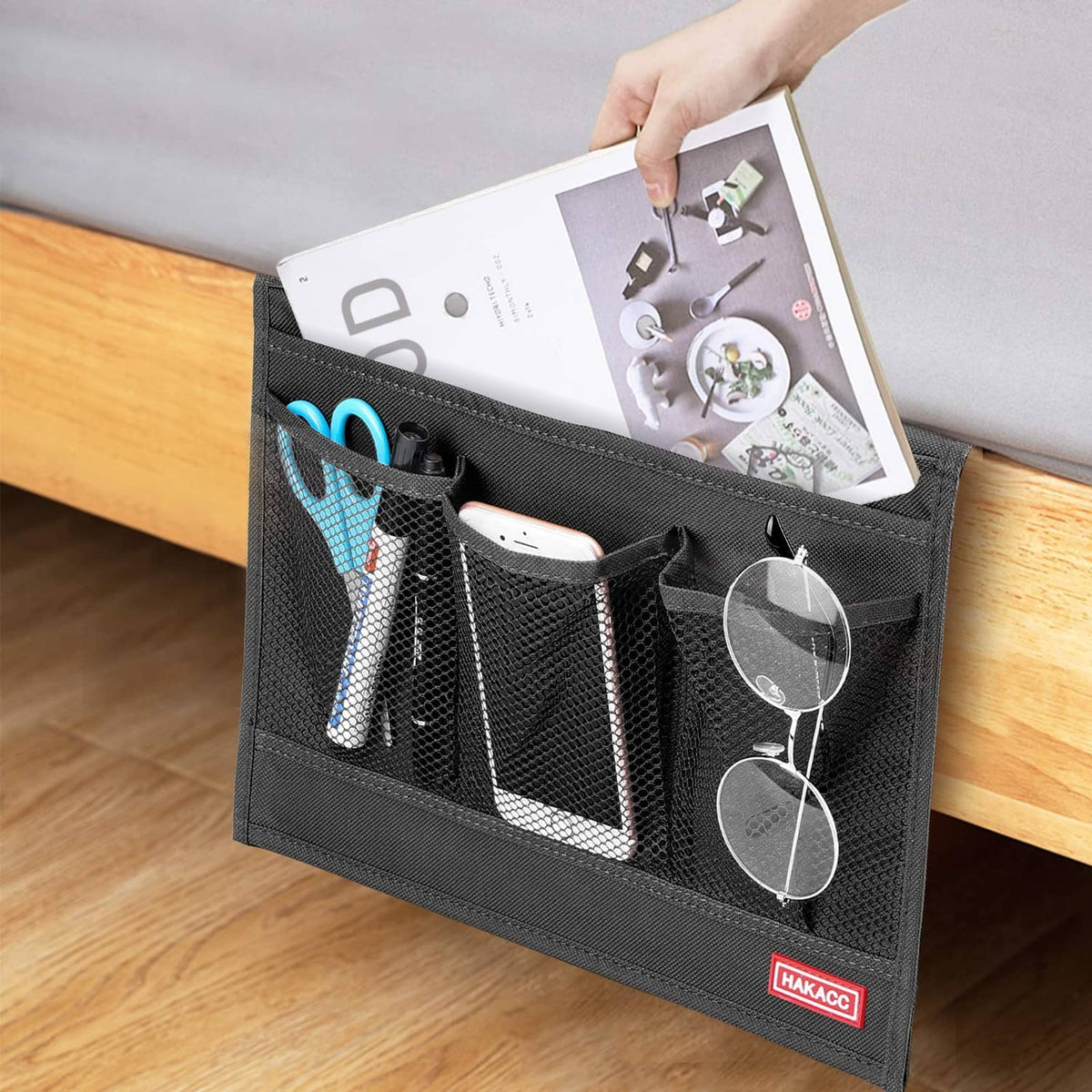 Black bedside storage caddy with mesh pockets holding a tablet and small items