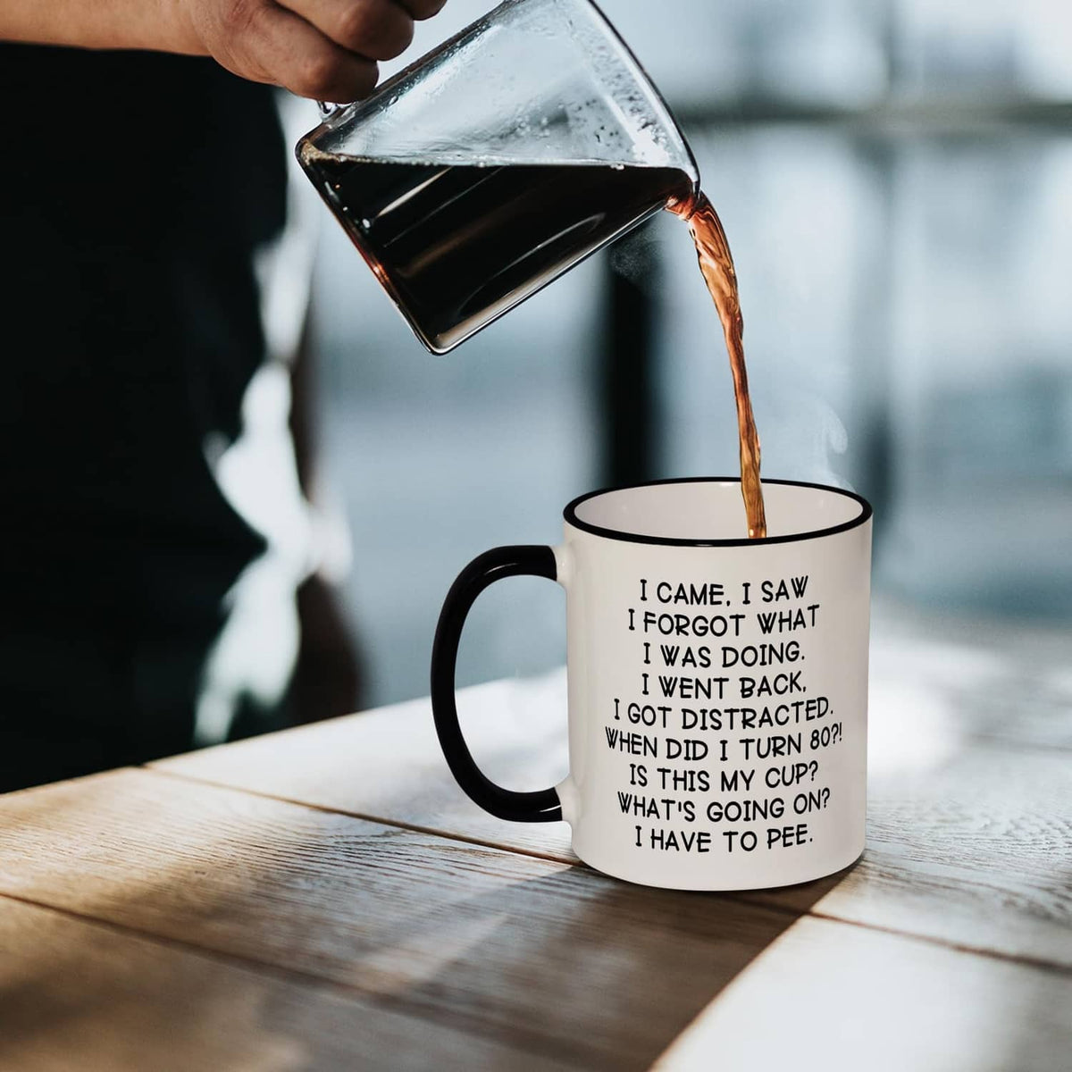 White mug with black handle and rim, 'turn 80' quote, dark liquid being poured.