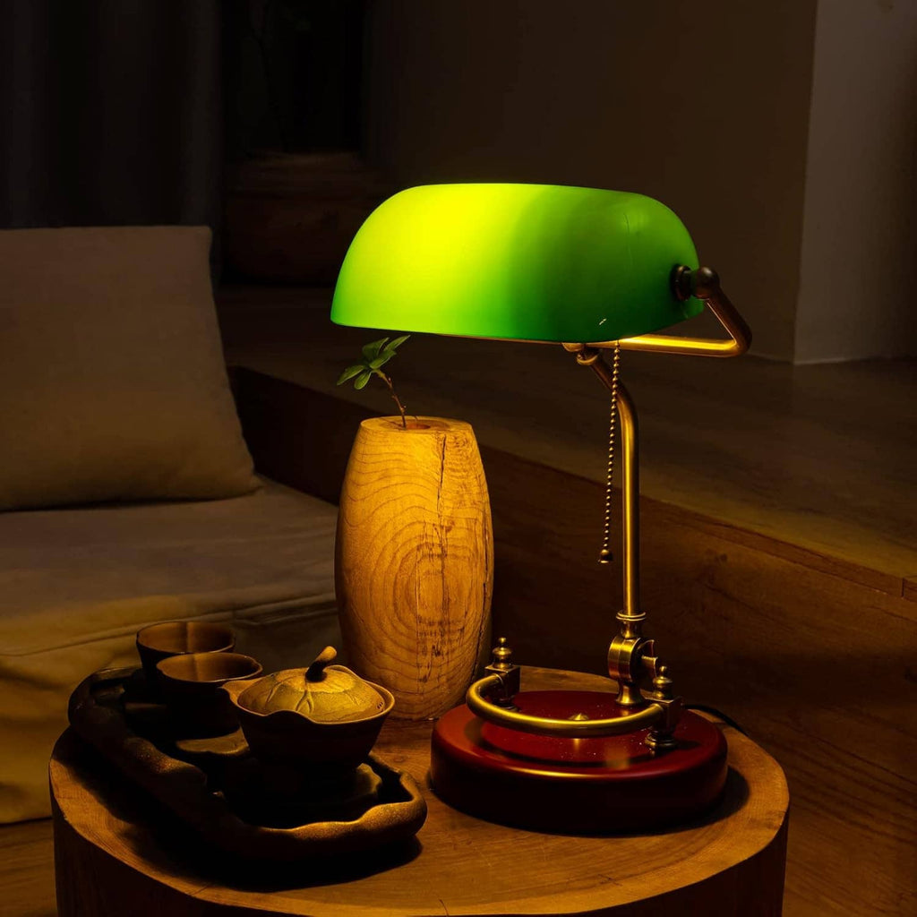Glowing green bankers desk lamp with brass frame and round red wood base