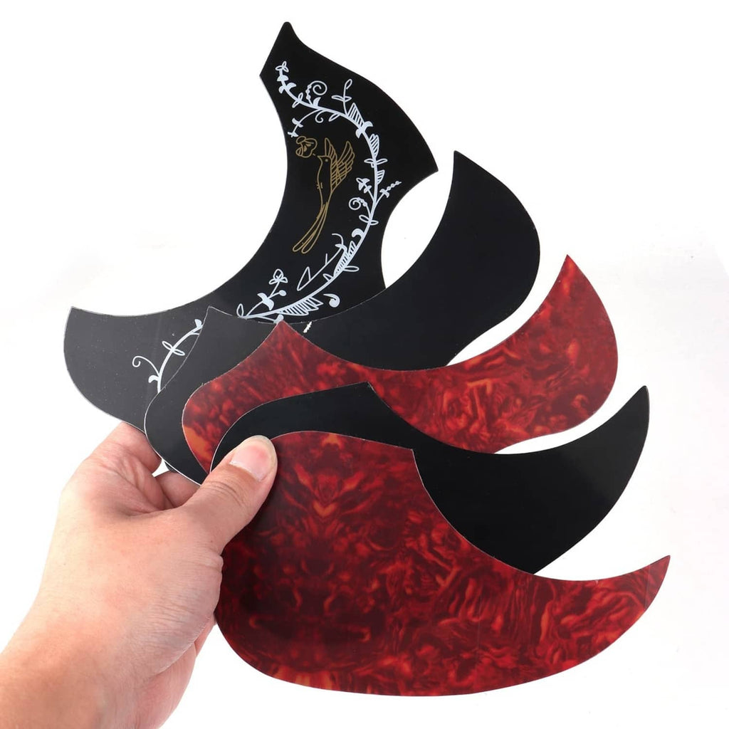 Self-adhesive acoustic guitar pickguards held in a hand, red and black with white design
