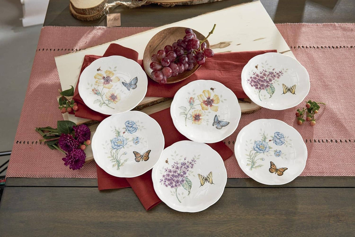 Six small round plates with butterfly and wildflower designs, arranged on serving linens
