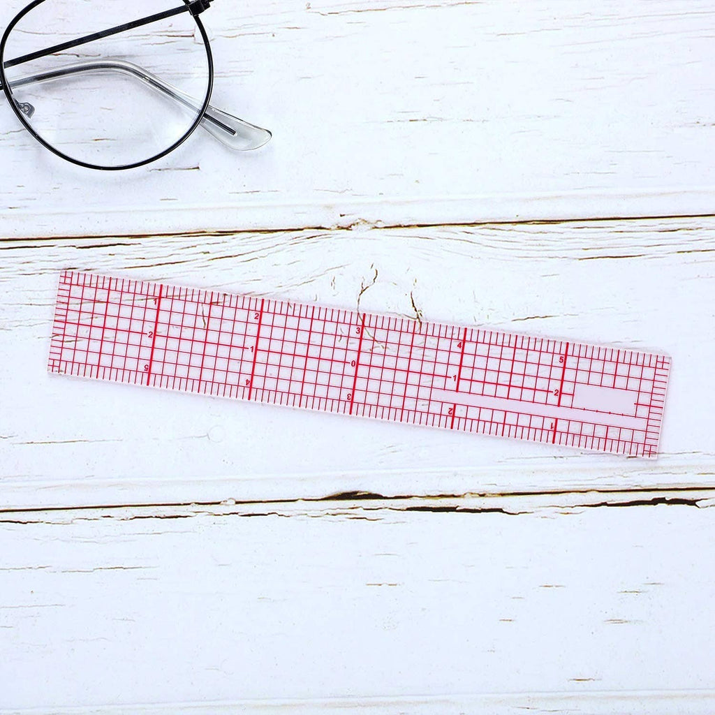 Clear plastic grid ruler with red measurement lines on a light wood surface