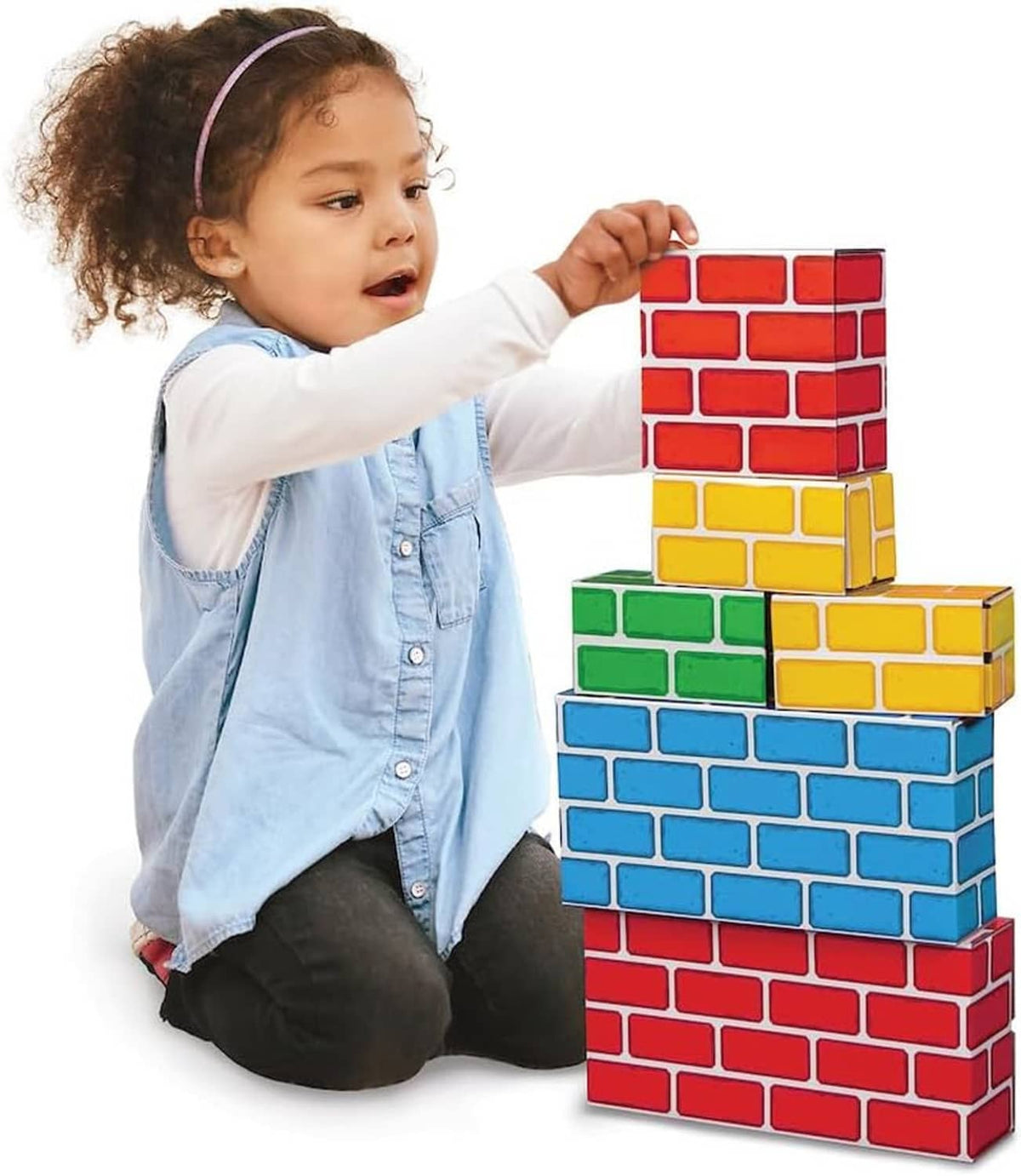Child kneeling next to tall stack of colorful cardboard brick blocks