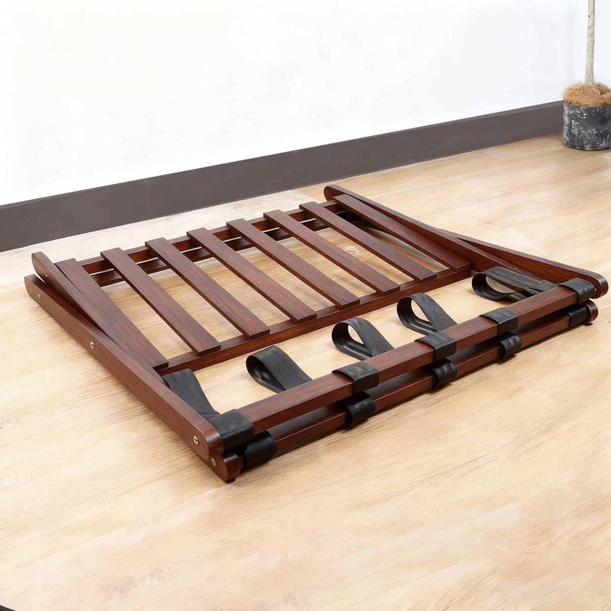 Folded wooden luggage rack base with slats and black strap accents, tabletop view