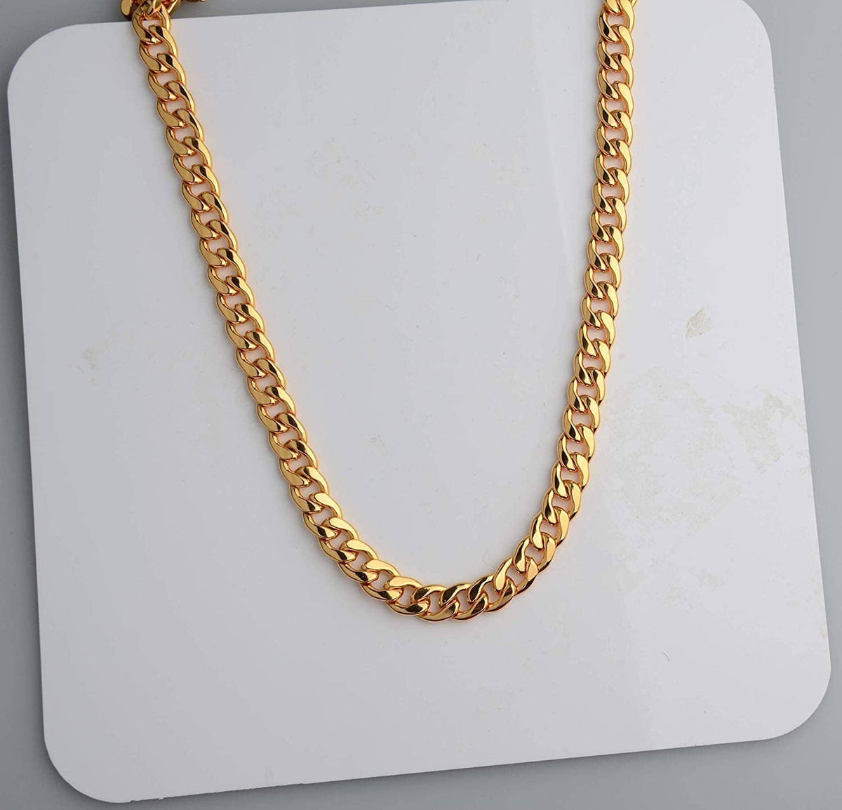 Gold curb-link chain necklace laid flat on a white display card